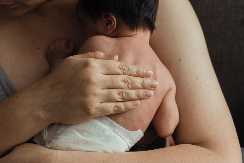 Mamă ținând nou-născutul pe piept în contact skin-to-skin